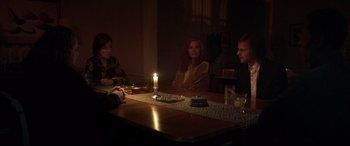 Movie still from “French Exit” (2020), directed by Azazel Jacobs – A group of people sitting around a table with a candle; Medium shot, Over the shoulder angle