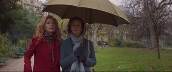 Movie still from “French Exit” (2020), directed by Azazel Jacobs – Two women standing under an umbrella in a park; Medium shot, Low angle