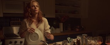 Movie still from “French Exit” (2020), directed by Azazel Jacobs – A woman holding a white plate in a kitchen; Medium shot, Low angle