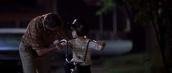 Movie still from “Frequency” (2000), directed by Gregory Hoblit – A young boy riding a bike at night while wearing a helmet; Medium shot, Over the shoulder angle