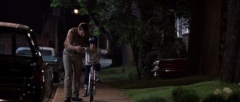 Movie still from “Frequency” (2000), directed by Gregory Hoblit – A man helping a child learn to ride a bike; Wide shot, Over the shoulder angle