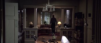 Movie still from “Frequency” (2000), directed by Gregory Hoblit – A man standing at a dining room table in front of a living room; Wide shot, High angle
