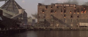 Movie still from “Frequency” (2000), directed by Gregory Hoblit – A building that has been set on fire by the water; Extreme Wide shot, High angle