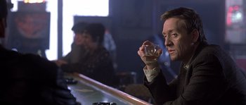 Movie still from “Frequency” (2000), directed by Gregory Hoblit – A man sitting at a bar holding a glass; Close Up shot, Over the shoulder angle