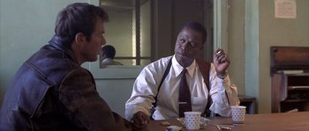 Movie still from “Frequency” (2000), directed by Gregory Hoblit – Two men are sitting at a table and one of them is smoking a cigarette; Medium shot, Over the shoulder angle