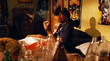 Movie still from “Friday” (1995), directed by F. Gary Gray – A man sitting on a bed smoking a cigarette; Medium shot, High angle