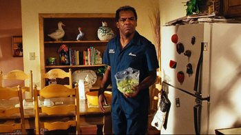 Movie still from “Friday” (1995), directed by F. Gary Gray – A man holding a bag of grapes in a kitchen; Medium shot, Low angle