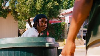 Movie still from “Friday” (1995), directed by F. Gary Gray – A young man is sitting in a trash can; Medium shot, Over the shoulder angle