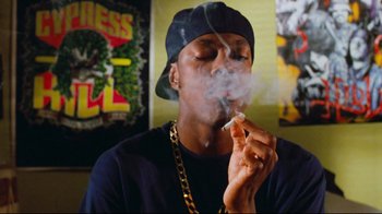Movie still from “Friday” (1995), directed by F. Gary Gray – A man smoking a cigarette while wearing a hat; Medium shot, Overhead angle