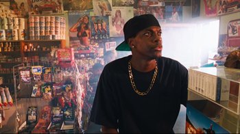 Movie still from “Friday” (1995), directed by F. Gary Gray – A man wearing a black shirt and a green hat; Medium shot, Over the shoulder angle