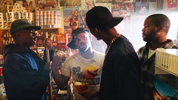 Movie still from “Friday” (1995), directed by F. Gary Gray – Two men talking in a room full of posters; Medium shot, Over the shoulder angle