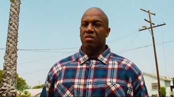 Movie still from “Friday” (1995), directed by F. Gary Gray – A man in a blue and red plaid shirt is standing outside; Close Up shot, Low angle