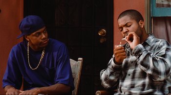 Movie still from “Friday” (1995), directed by F. Gary Gray – Two young men sitting at a table and one is eating a donut; Medium shot, Over the shoulder angle