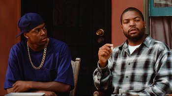 Movie still from “Friday” (1995), directed by F. Gary Gray – Two men sitting next to each other in front of a door; Medium shot, Over the shoulder angle
