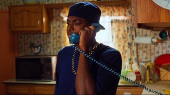 Movie still from “Friday” (1995), directed by F. Gary Gray – A man talking on a phone while wearing a blue hat; Medium shot, Low angle