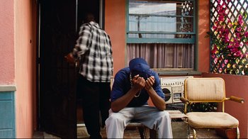 Movie still from “Friday” (1995), directed by F. Gary Gray – A man sitting in front of a door with his head down; Wide shot, High angle
