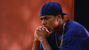 Movie still from “Friday” (1995), directed by F. Gary Gray – A man in a blue shirt and a hat is sitting down; Close Up shot, High angle