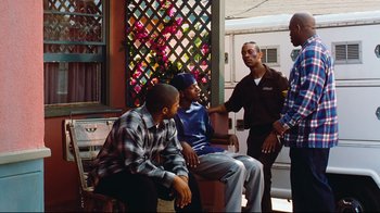 Movie still from “Friday” (1995), directed by F. Gary Gray – A group of young men sitting next to each other on a porch; Medium shot, Over the shoulder angle