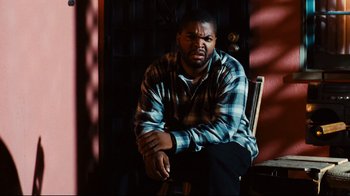 Movie still from “Friday” (1995), directed by F. Gary Gray – A man sitting on a chair in a room; Medium shot, High angle