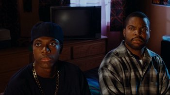 Movie still from “Friday” (1995), directed by F. Gary Gray – A couple of men sitting next to each other in front of a tv; Medium shot, High angle