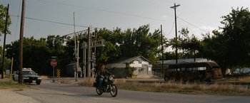 Movie still from “Friday the 13th” (2009), directed by Marcus Nispel – A man riding a motorcycle down the middle of the street; Extreme Wide shot, Over the shoulder angle