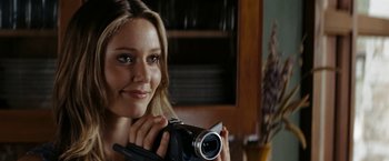Movie still from “Friday the 13th” (2009), directed by Marcus Nispel – A beautiful young lady holding a camera and smiling for the camera; Close Up shot, Over the shoulder angle