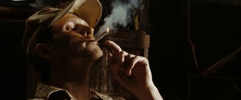 Movie still from “Friday the 13th” (2009), directed by Marcus Nispel – A man smoking a cigarette while wearing a baseball cap; Close Up shot, Low angle