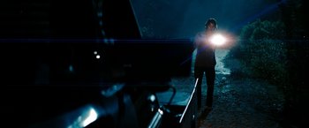 Movie still from “Friday the 13th” (2009), directed by Marcus Nispel – A man standing in the dark holding a flashlight; Wide shot, Over the shoulder angle