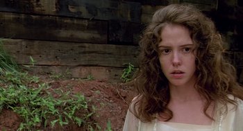 A young woman with long curly brown hair standing in front of a wooden wall