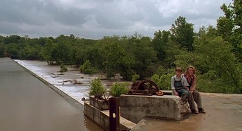 Movie still from “Fried Green Tomatoes” (1991), directed by Jon Avnet – A man sitting on the side of a river near trees; Extreme Wide shot, High angle