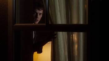 Movie still from “Fright Night” (2011), directed by Craig Gillespie – A young man looking out a window at the light; Medium shot, Low angle