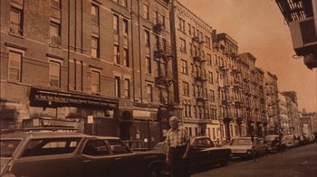 Movie still from “Fritz the Cat” (1972), directed by Ralph Bakshi – An older man standing in front of a row of parked cars; Wide shot, High angle
