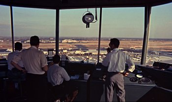 Movie still from “From Russia with Love” (1963), directed by Terence Young – A group of men standing in a control tower looking out at an airport; Extreme Wide shot, Low angle