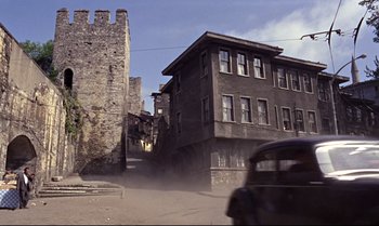Movie still from “From Russia with Love” (1963), directed by Terence Young – An old car driving down a street next to an old building; Extreme Wide shot, High angle