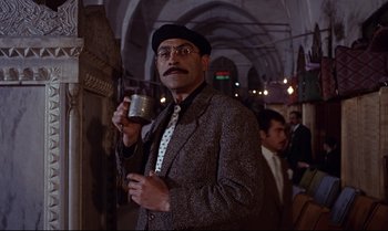 Movie still from “From Russia with Love” (1963), directed by Terence Young – A man in a suit and tie holding a cup; Medium shot, Low angle