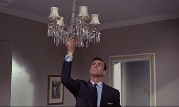 Movie still from “From Russia with Love” (1963), directed by Terence Young – A man in a suit and tie holding up a chandelier; Medium shot, Low angle