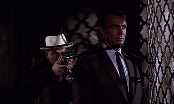 Movie still from “From Russia with Love” (1963), directed by Terence Young – A man holding a gun while standing next to another man in a suit; Medium shot, Low angle