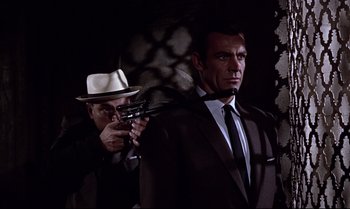 Movie still from “From Russia with Love” (1963), directed by Terence Young – A man holding a gun while standing next to another man in a suit; Medium shot, Low angle
