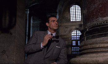 Movie still from “From Russia with Love” (1963), directed by Terence Young – A man in a suit and tie holding a pair of sunglasses; Medium shot, Low angle
