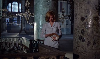 Movie still from “From Russia with Love” (1963), directed by Terence Young – A woman in a white shirt is holding a book; Medium shot, Low angle