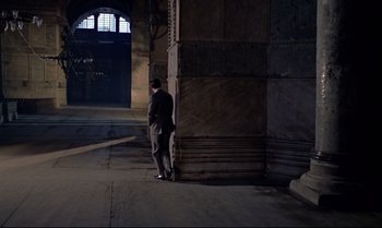 Movie still from “From Russia with Love” (1963), directed by Terence Young – A man leaning against a wall in a dark room; Extreme Wide shot, High angle