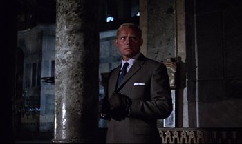 Movie still from “From Russia with Love” (1963), directed by Terence Young – A man in a suit and tie standing next to a pillar; Medium shot, Low angle