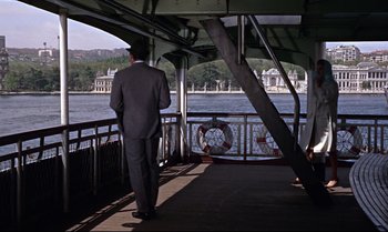 Movie still from “From Russia with Love” (1963), directed by Terence Young – A man in a suit standing on a boat looking out over the water; Wide shot, Over the shoulder angle
