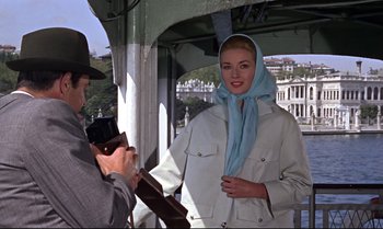Movie still from “From Russia with Love” (1963), directed by Terence Young – A man taking a picture of a woman wearing a white jacket and a blue scarf; Medium shot, Low angle