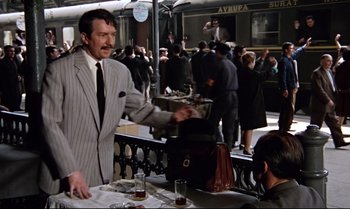 Movie still from “From Russia with Love” (1963), directed by Terence Young – A man wearing a suit and tie standing at a table; Wide shot, Over the shoulder angle