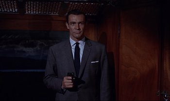 Movie still from “From Russia with Love” (1963), directed by Terence Young – A man in a suit and tie holding a gun; Medium shot, Low angle