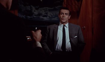 Movie still from “From Russia with Love” (1963), directed by Terence Young – A man wearing a suit and tie holding a cigarette; Medium shot, Over the shoulder angle