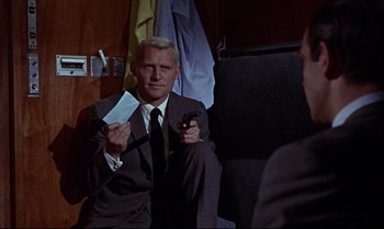 Movie still from “From Russia with Love” (1963), directed by Terence Young – A man in a suit and tie holding a cell phone; Medium shot, Over the shoulder angle