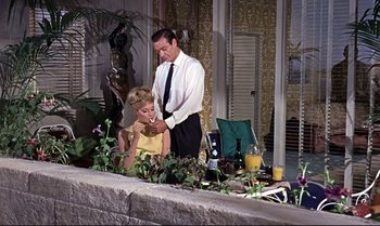 Movie still from “From Russia with Love” (1963), directed by Terence Young – A man and a woman sitting in front of plants; Medium shot, Low angle
