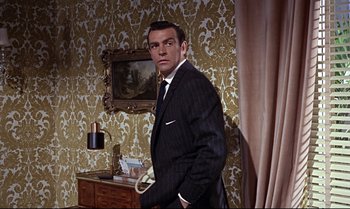 Movie still from “From Russia with Love” (1963), directed by Terence Young – A man in a suit standing next to a table; Medium shot, High angle